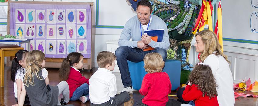 Man holding book talking to children sitting on the floor.