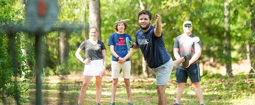 在美国，一名男学生和一群打飞盘高尔夫球的学生一起扔飞盘.