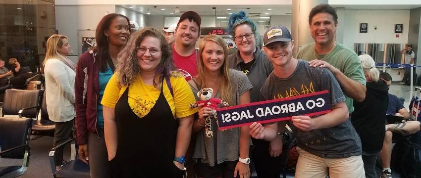 students standing together in an airport terminal holding a "go abroad jags" banner